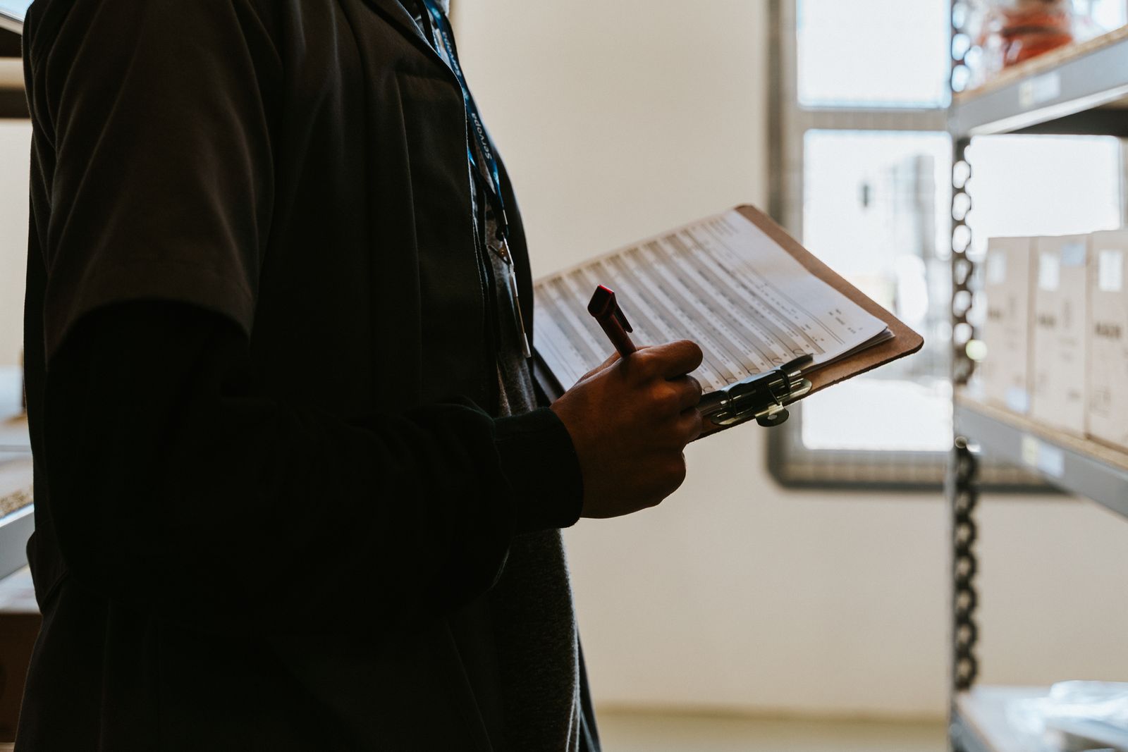 Stock photograph of a worker checking inventory on a clipboard beside warehouse shelves