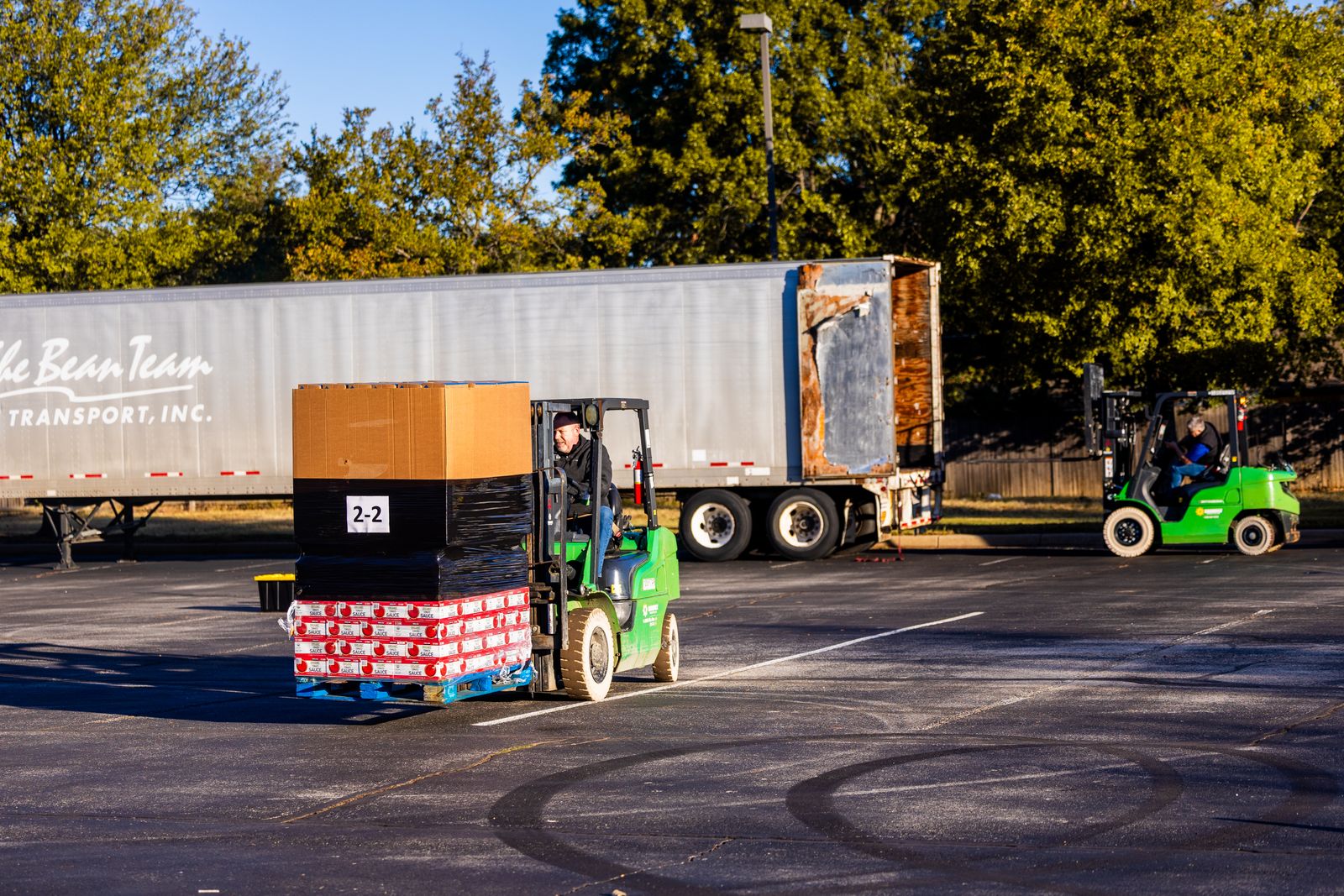Stock photograph of forklift operators moving wrapped grocery pallets beside a freight trailer